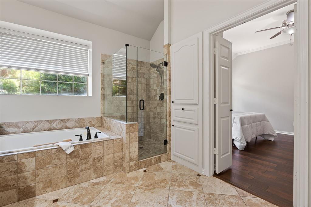 Bathroom featuring a drop-in soaking tub and glass-enclosed shower with tiled surround, stone-finish tile flooring, and custom cabinetry with matte black hardware