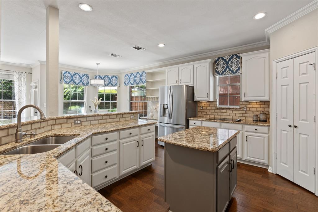 Kitchen featuring stone countertops, white cabinetry, a center island, brick-style tile backsplash, and wood-finish flooring