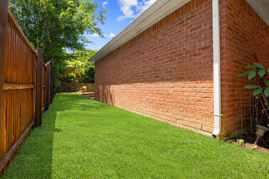 Exterior side yard featuring a brick facade, full-height privacy fencing, and a manicured lawn