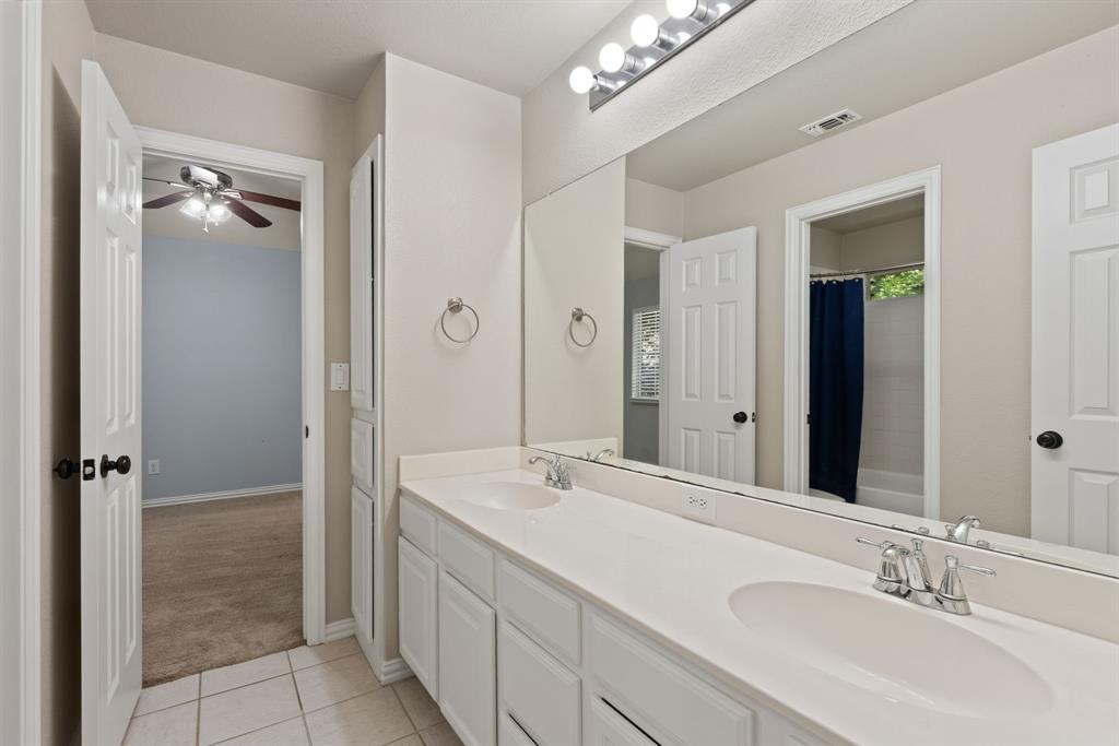 Double vanity featuring dual integrated sinks, white cabinetry, a full-width mirror, and a multi-bulb light fixture