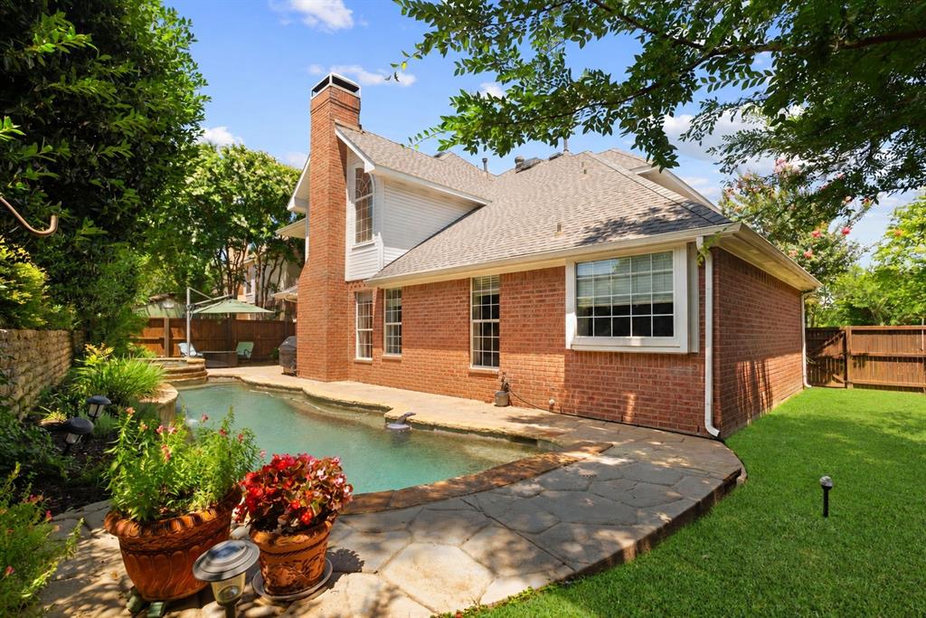 Brick exterior with an external chimney, flagstone patio, in-ground swimming pool, and landscaped yard enclosed by wood fencing
