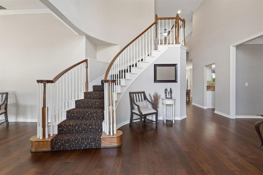 Grand foyer featuring a curved staircase with a wood handrail, white balusters, and a tiered landing Grand foyer featuring a curved staircase with a wood handrail, white balusters, and a tiered landing