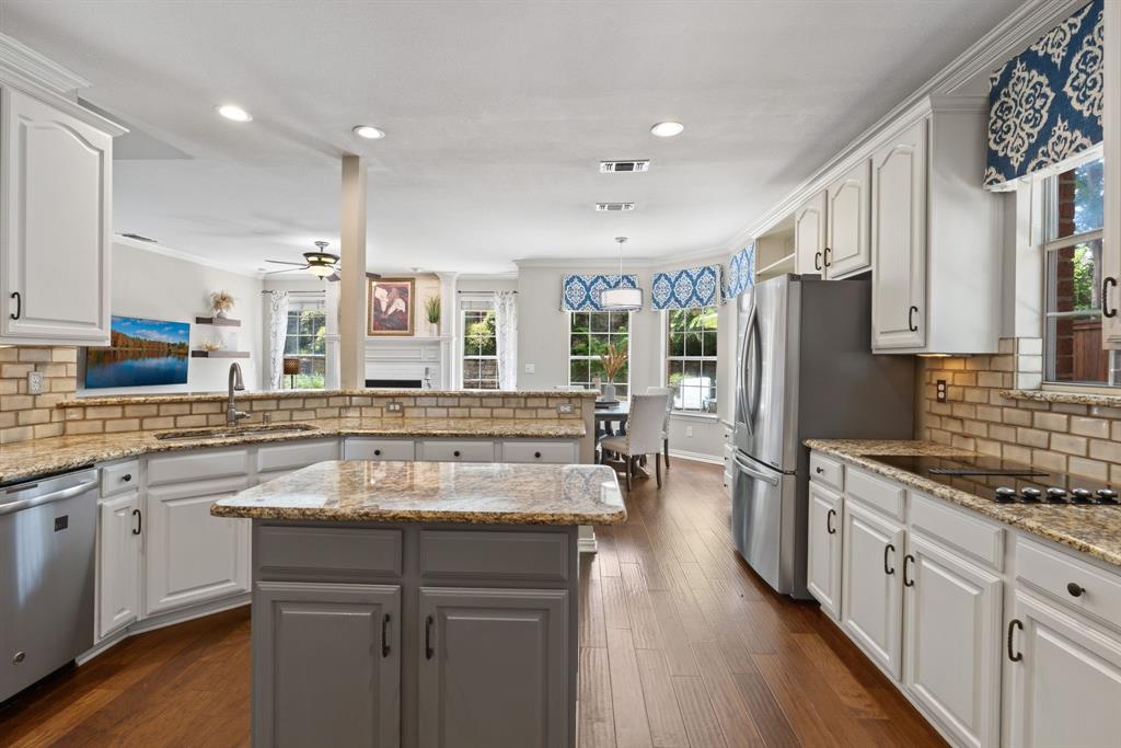 Kitchen featuring custom white cabinetry, stone countertops, brick-style tile backsplash, wood-finish flooring, and a central island with a contrasting finish