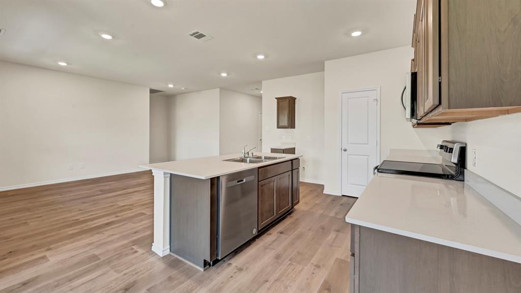 Open concept kitchen featuring an island with integrated sink, stainless steel dishwasher, light-toned countertops, and wood-finish flooring