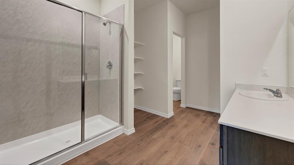 Spa-inspired primary bathroom featuring a frameless glass shower enclosure with chrome hardware, white subway tile surround, and a white vanity with integrated sink