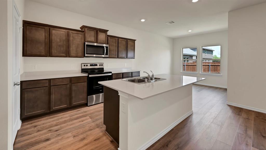 Kitchen featuring dark wood-finish cabinetry, stainless steel appliances, a white island with a double sink, and wood-finish flooring