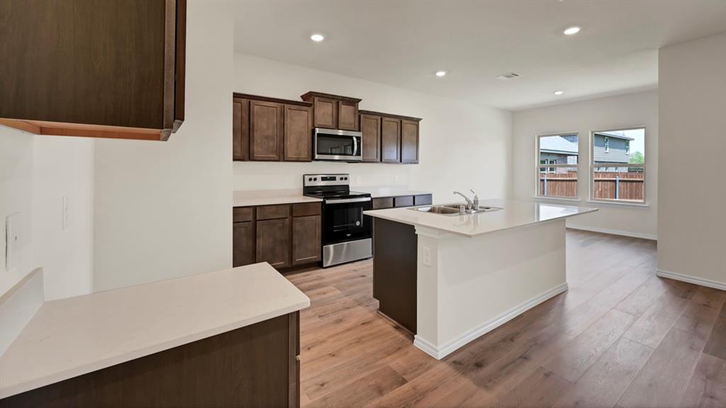 Kitchen featuring wood-finish flooring, recessed lighting, white countertops, dark wood cabinetry, and stainless steel appliances