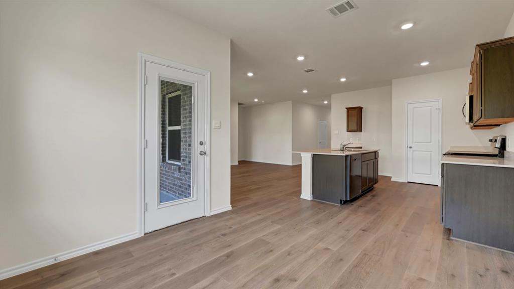 Wood-finish flooring throughout, recessed lighting, kitchen island with sink, white shaker style cabinetry with dark hardware, and a glass-paneled exterior door