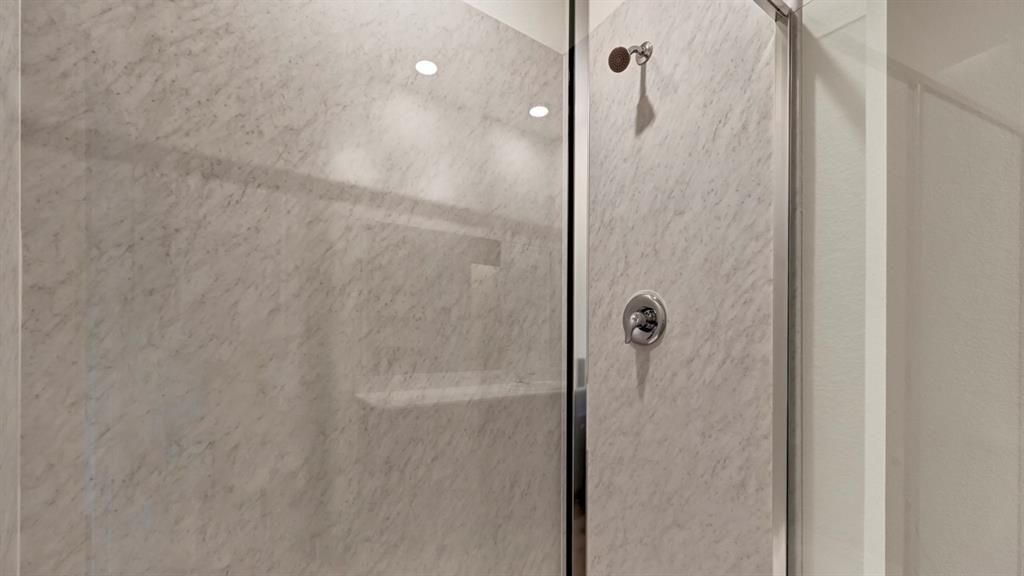Glass-enclosed shower with a polished chrome shower head, chrome control handle, and recessed lighting