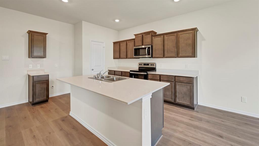 Expansive kitchen island with an undermount double-basin sink, wood-finish flooring, dark wood cabinetry, and stainless steel appliances