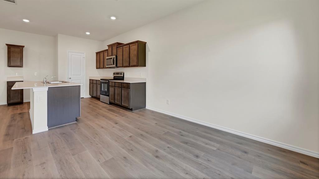 Kitchen featuring wood-finish flooring, recessed lighting, dark wood cabinetry, stainless steel appliances, and an island with a built-in sink and countertop