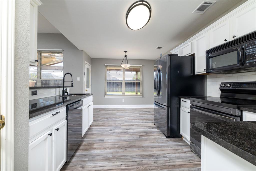 Kitchen featuring white cabinetry, dark stone countertops, wood-finish flooring, a matte black faucet, and built-in black appliances
