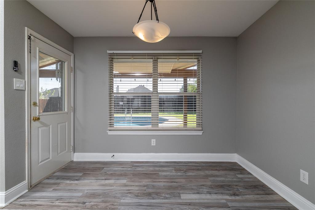 Wood-finish flooring, neutral wall tones, multi-pane window with horizontal blinds, glass-panel exterior door, and pendant lighting fixture