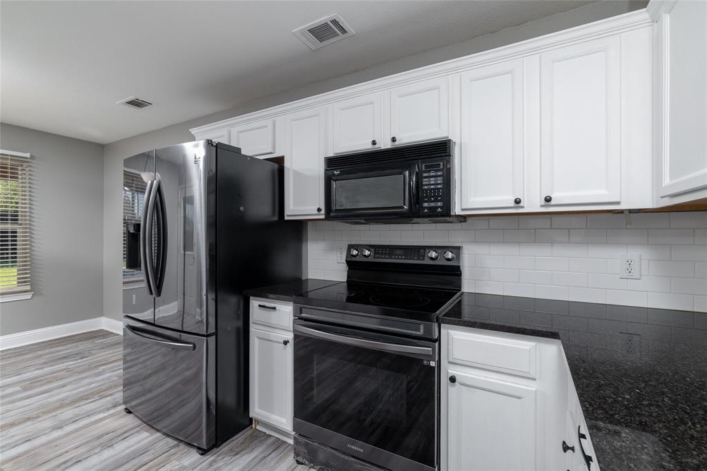 Kitchen featuring white shaker-style cabinetry, dark stone countertops, white subway tile backsplash, and stainless steel appliances