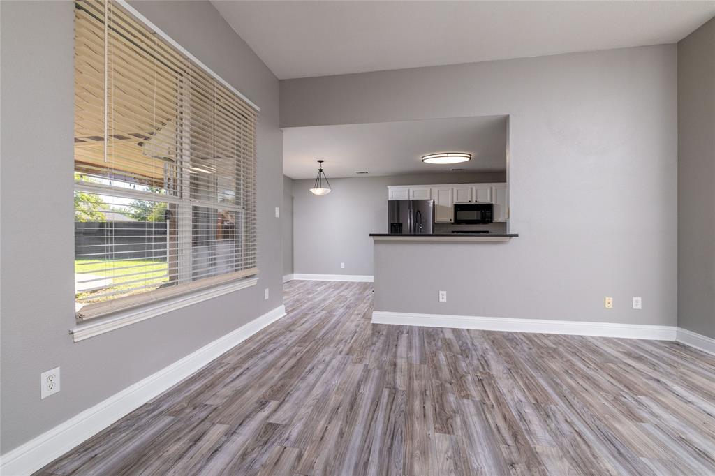 Wood-finish flooring, large window with horizontal blinds, pass-through opening to kitchen, and breakfast bar