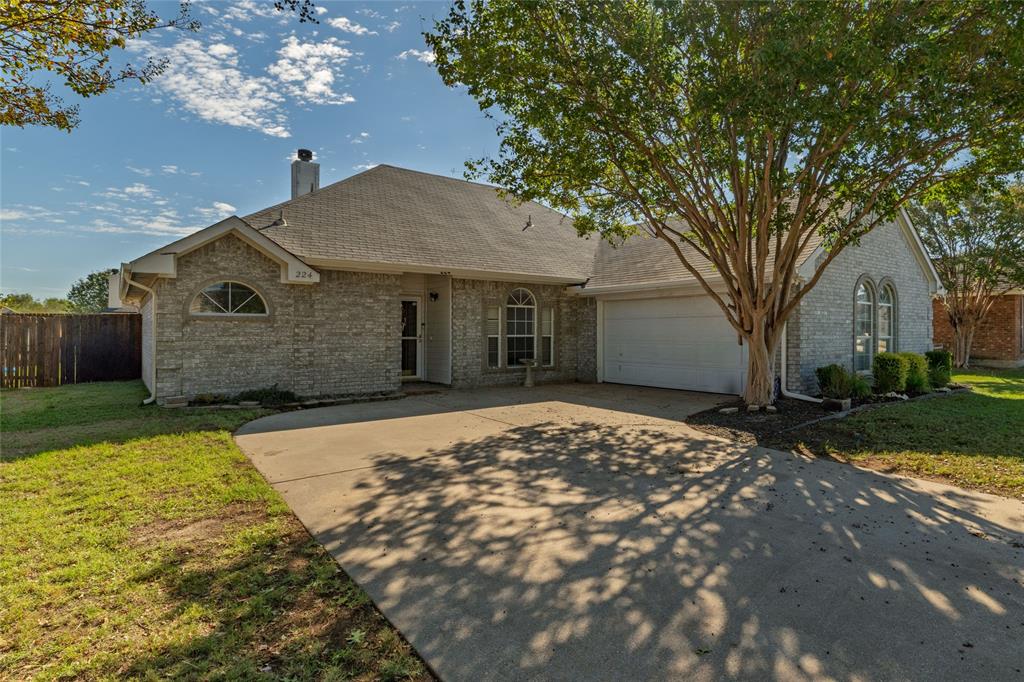 Single-story brick exterior featuring an arched window, attached two-car garage, concrete driveway, and mature landscaping Single-story brick exterior featuring an arched window, attached two-car garage, concrete driveway, and mature landscaping