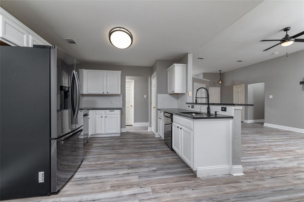 Kitchen featuring white cabinetry, dark countertops, wood-finish flooring, a matte black faucet, and stainless steel appliances