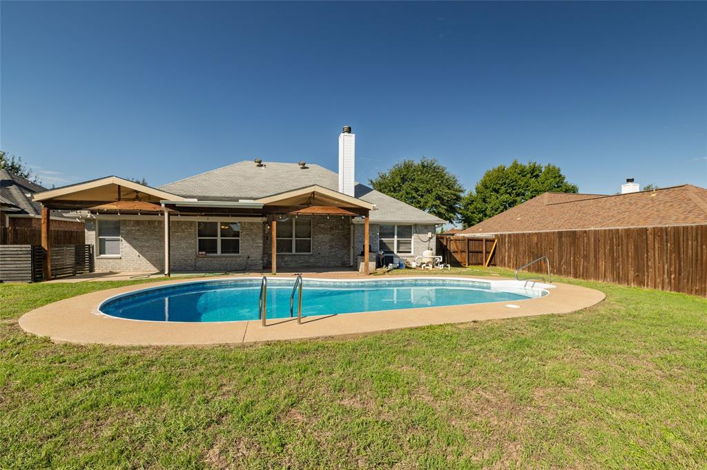 Backyard featuring an in-ground swimming pool, concrete pool deck, covered patio with wood supports, brick exterior, and wood privacy fencing