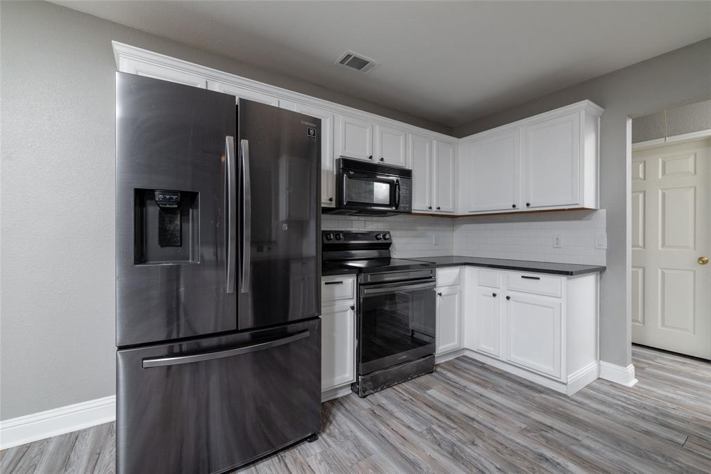 Kitchen featuring white shaker-style cabinetry, dark stone-finish countertops, wood-finish flooring, and black stainless steel appliances