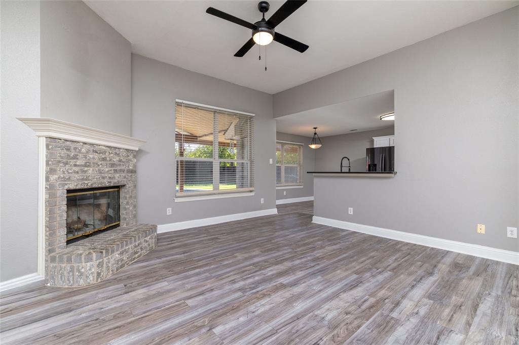Living area featuring wood-finish flooring, a brick fireplace with a mantel, and a black ceiling fan Living area featuring wood-finish flooring, a brick fireplace with a mantel, and a black ceiling fan