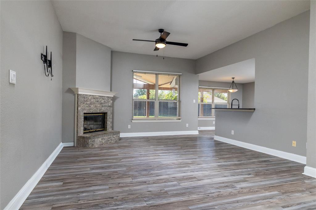 Living area featuring wood-finish flooring, stone-surround fireplace with mantel, ceiling fan, and bar-style pass-through Living area featuring wood-finish flooring, stone-surround fireplace with mantel, ceiling fan, and bar-style pass-through