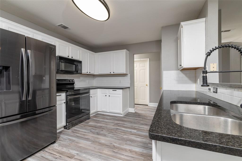 Kitchen featuring white shaker-style cabinetry, dark stone-finish countertops, subway tile backsplash, wood-finish flooring, and black appliances
