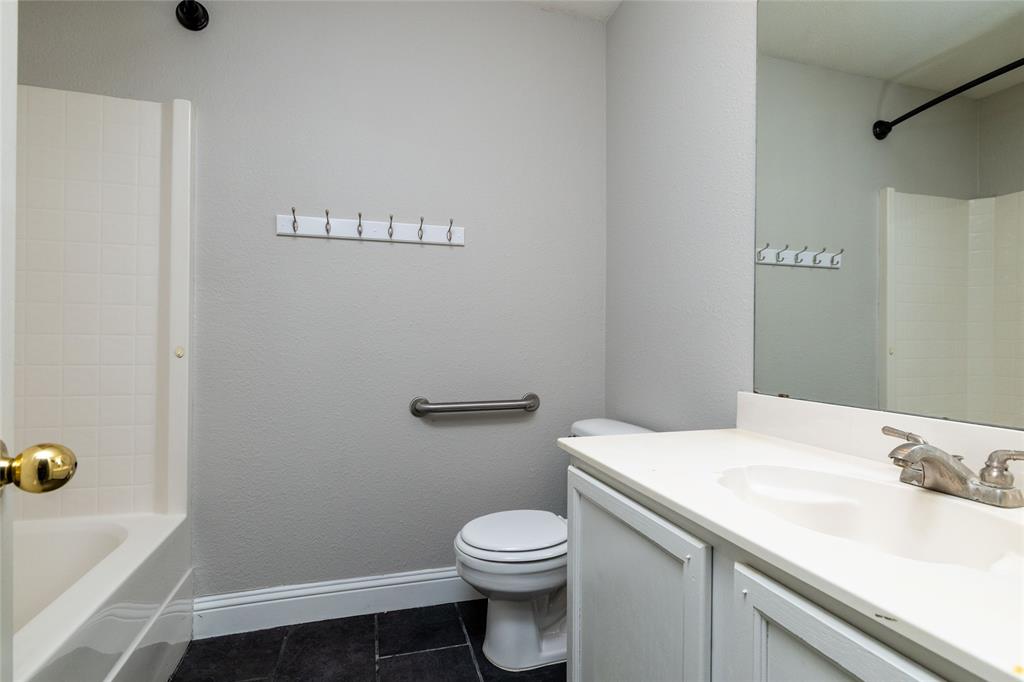 Full-width vanity featuring an integrated sink, polished metal faucet, white cabinetry, and a large wall-mounted mirror, paired with a shower-tub combination featuring tiled surround and a metal grab bar