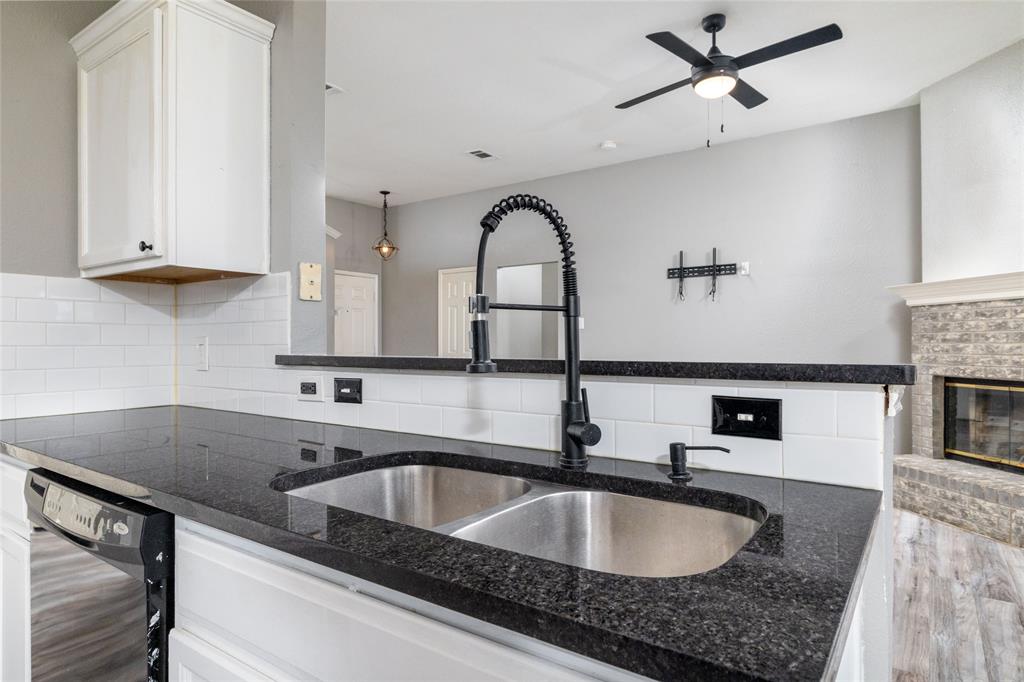 Kitchen featuring dark stone countertops, white subway tile backsplash, stainless steel dual-basin sink, matte black gooseneck faucet, and white cabinetry