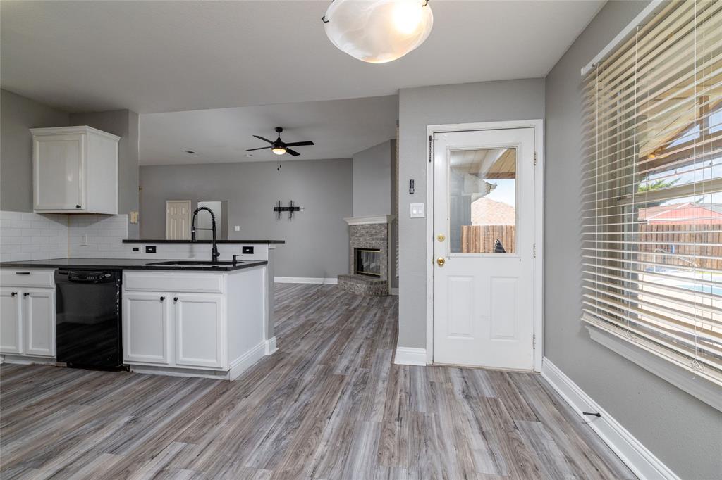 Kitchen featuring white cabinetry, dark countertops, a black pull-down faucet, wood-finish flooring, and a stone-surround fireplace