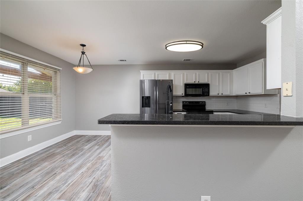 Kitchen featuring white cabinetry, dark stone-style countertops, stainless steel refrigerator, built-in microwave, and wood-finish flooring