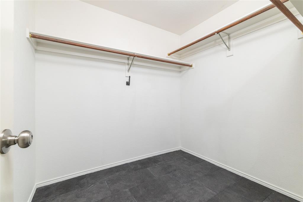Walk-in storage space featuring dark tile flooring, neutral wall finishes, and tiered hanging rods with integrated shelving