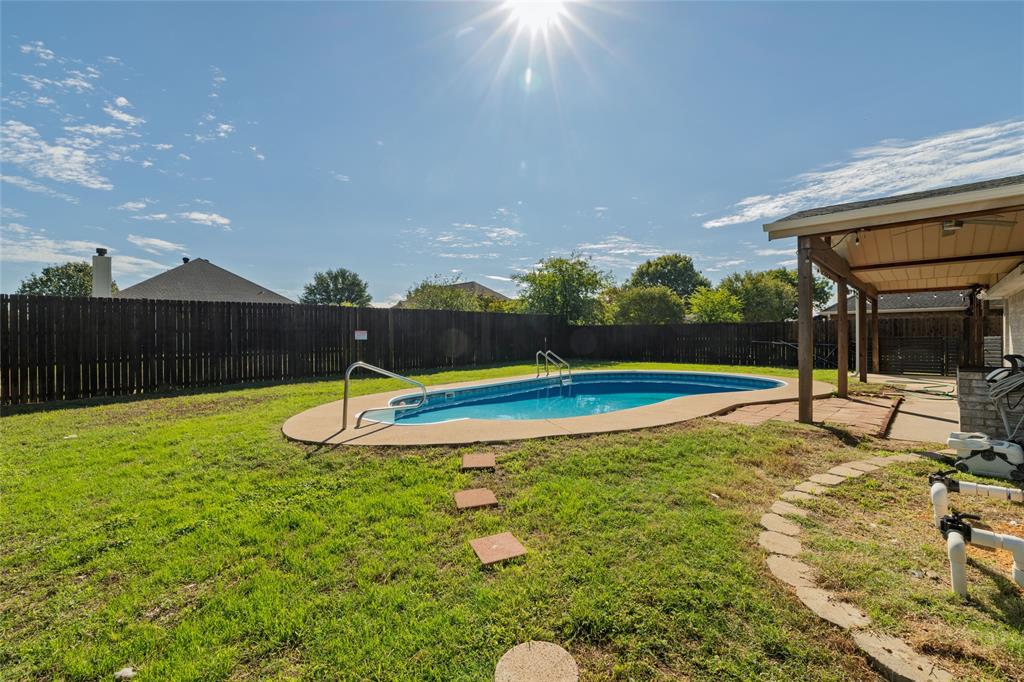 Private backyard featuring an in-ground swimming pool, concrete decking, covered patio, and wood privacy fencing