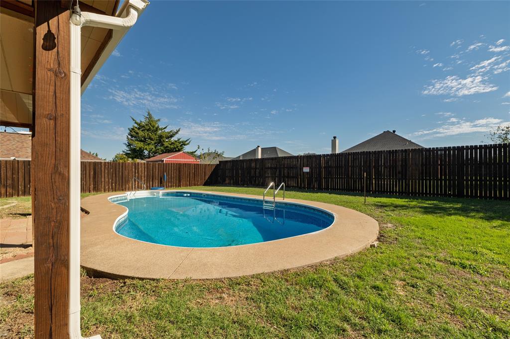 In-ground kidney-shaped swimming pool with a concrete surround, enclosed by a full-perimeter wood privacy fence and featuring a grassy lawn