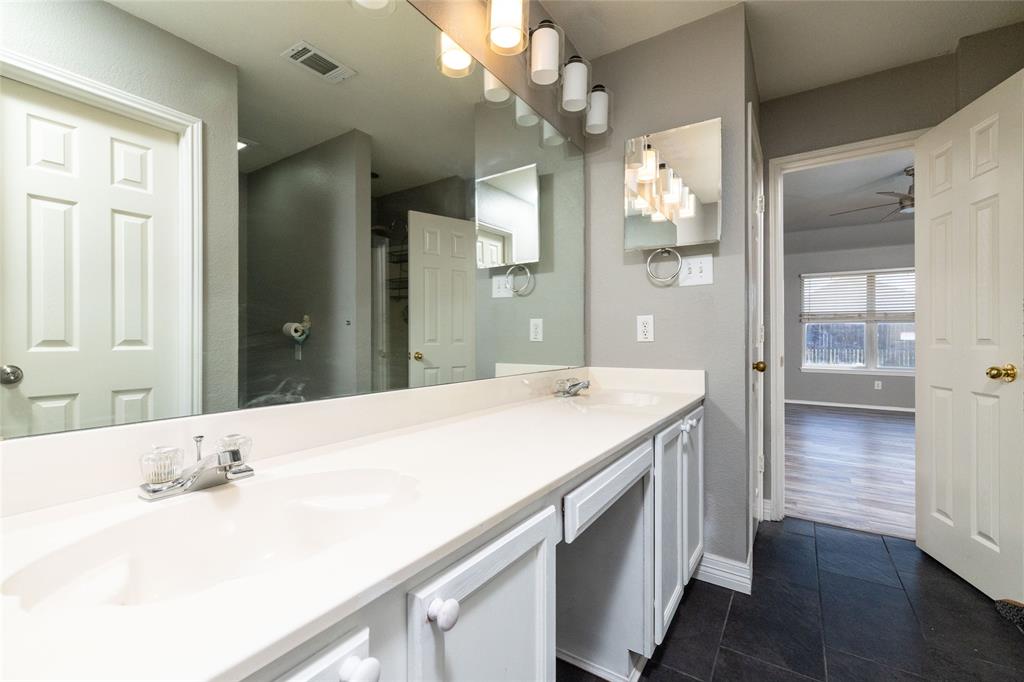 Dual-sink vanity with a solid-surface countertop, full-width wall mirror, five-light fixture, and dark-toned flooring