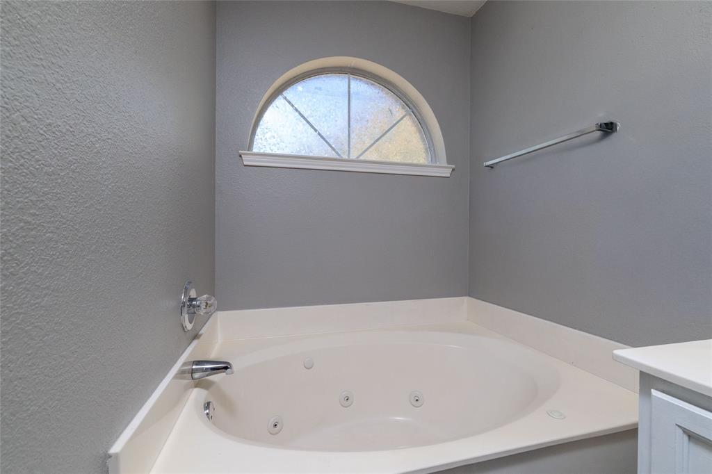 Oval jetted soaking tub with a solid-surface deck, arched window with a fanlight design, and a metallic wall-mounted towel bar