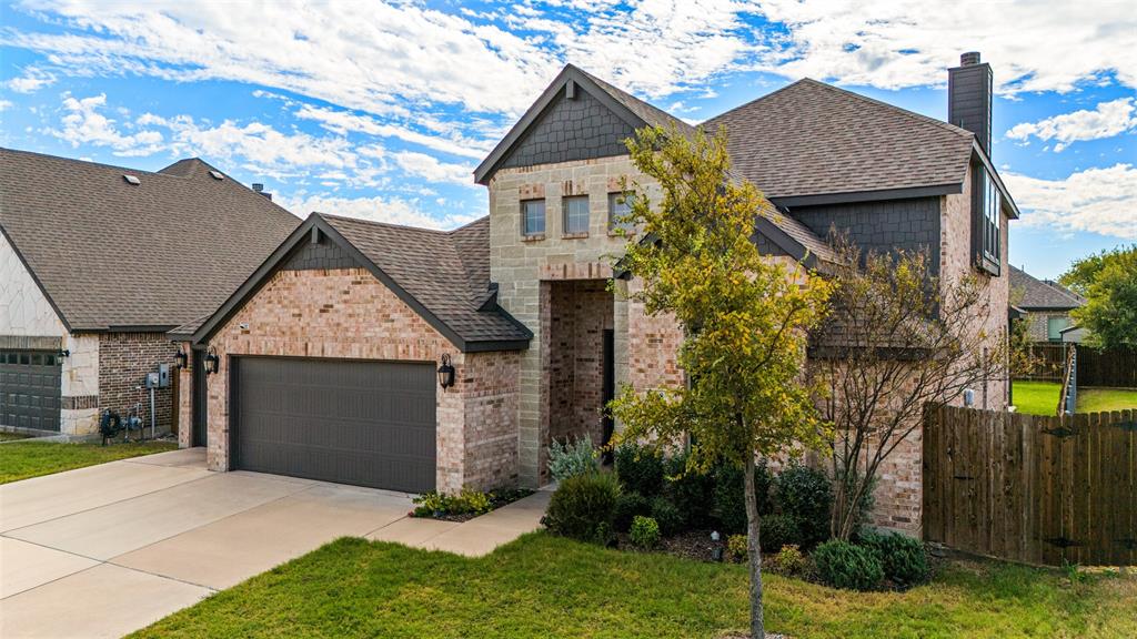 Two-story exterior featuring a brick and stone facade, dark shingle roof, integrated two-car garage, and cedar privacy fencing