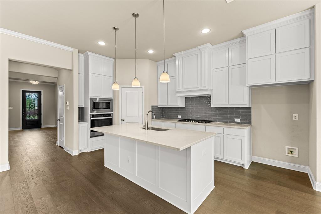 Kitchen featuring white cabinetry, quartz countertops, a grey subway tile backsplash, built-in stainless steel double ovens, and a center island with pendant lighting
