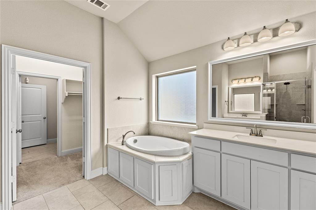 Bathroom featuring a drop-in soaking tub with a tiled surround, a large framed vanity mirror, white cabinetry with a light-toned countertop, and recessed lighting