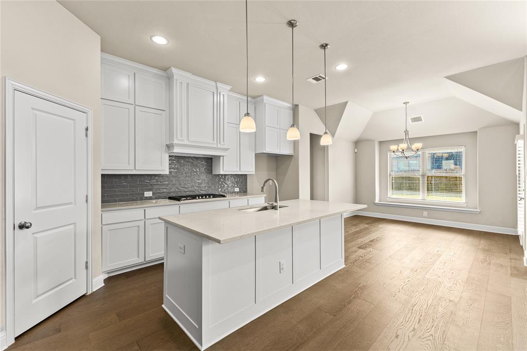 Kitchen featuring white shaker-style cabinetry, quartz countertops, a grey subway tile backsplash, pendant lighting, and wood-finish flooring