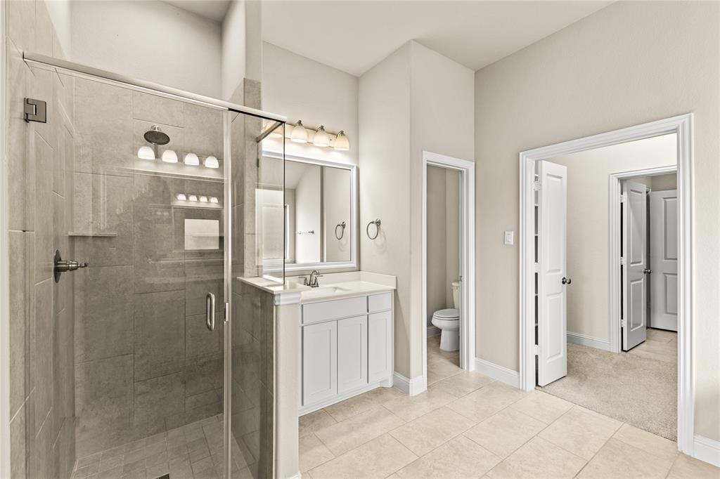 Walk-in shower with stone-tile surround, vanity with cabinetry and integrated countertop, framed vanity mirror, and tile flooring