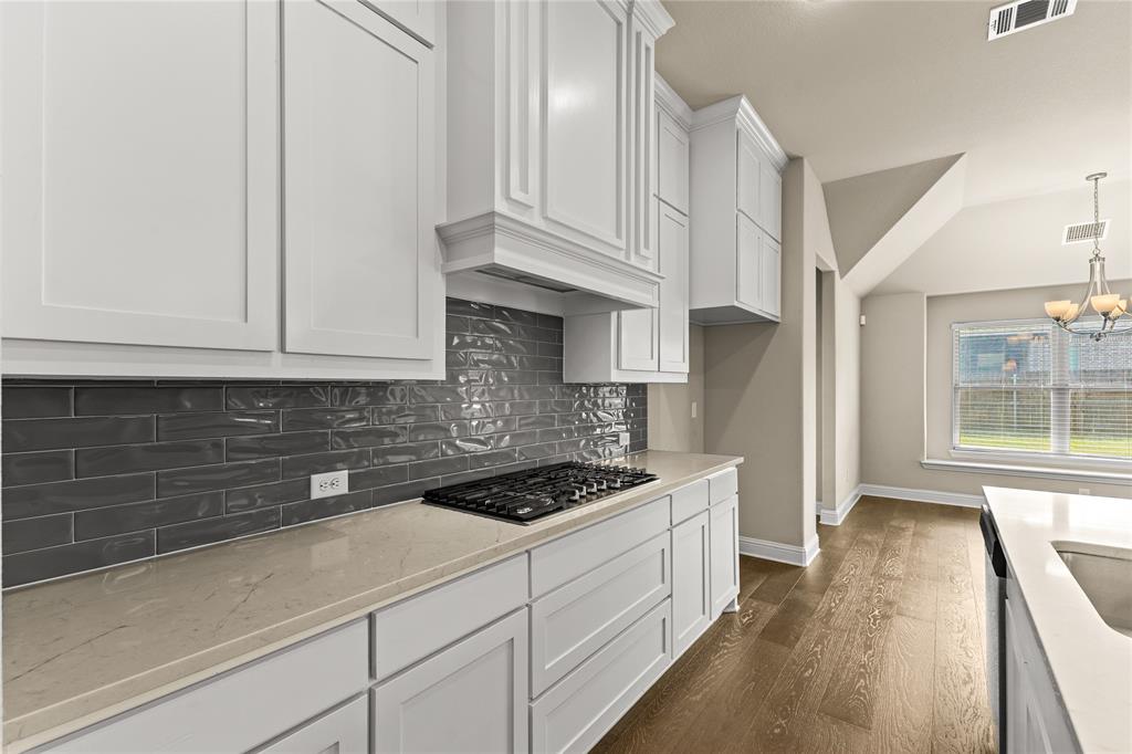 Kitchen featuring white shaker-style cabinetry, quartz countertops, a charcoal-toned subway tile backsplash, gas cooktop, and wood-finish flooring
