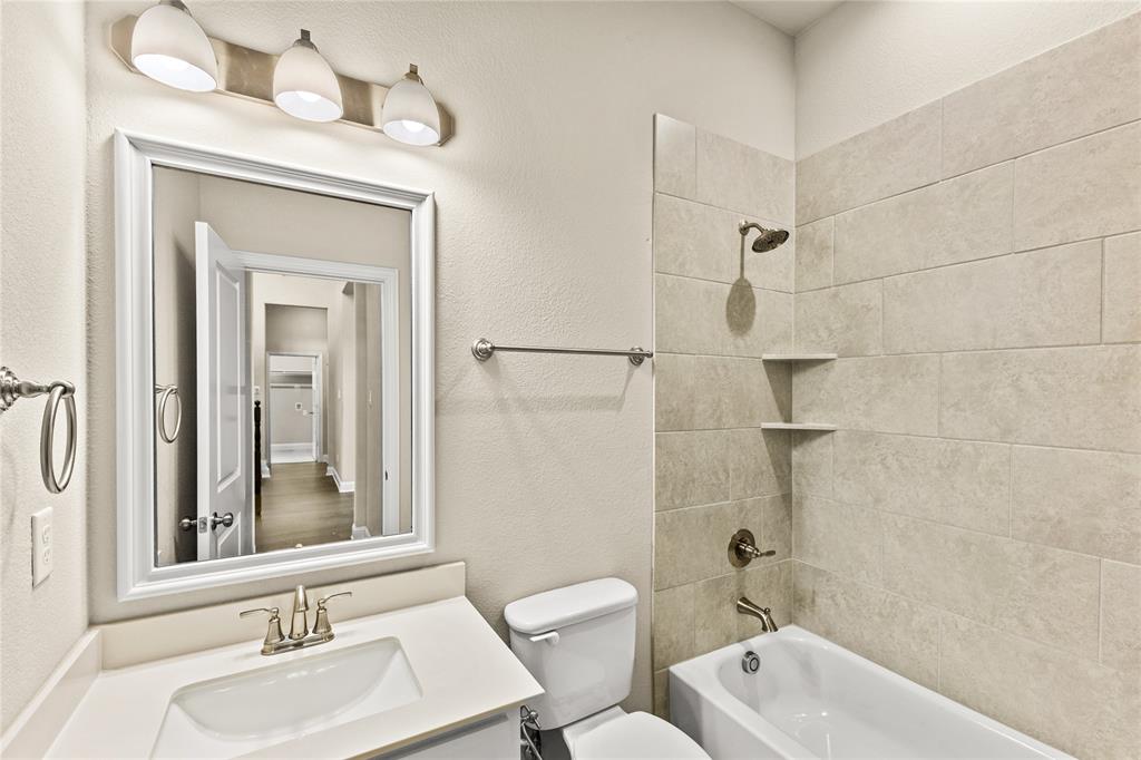 Bathroom featuring a vanity with a white countertop and drop-in basin, three-light fixture, framed mirror, and a tub-shower combination with floor-to-ceiling neutral tile surround and integrated shelving