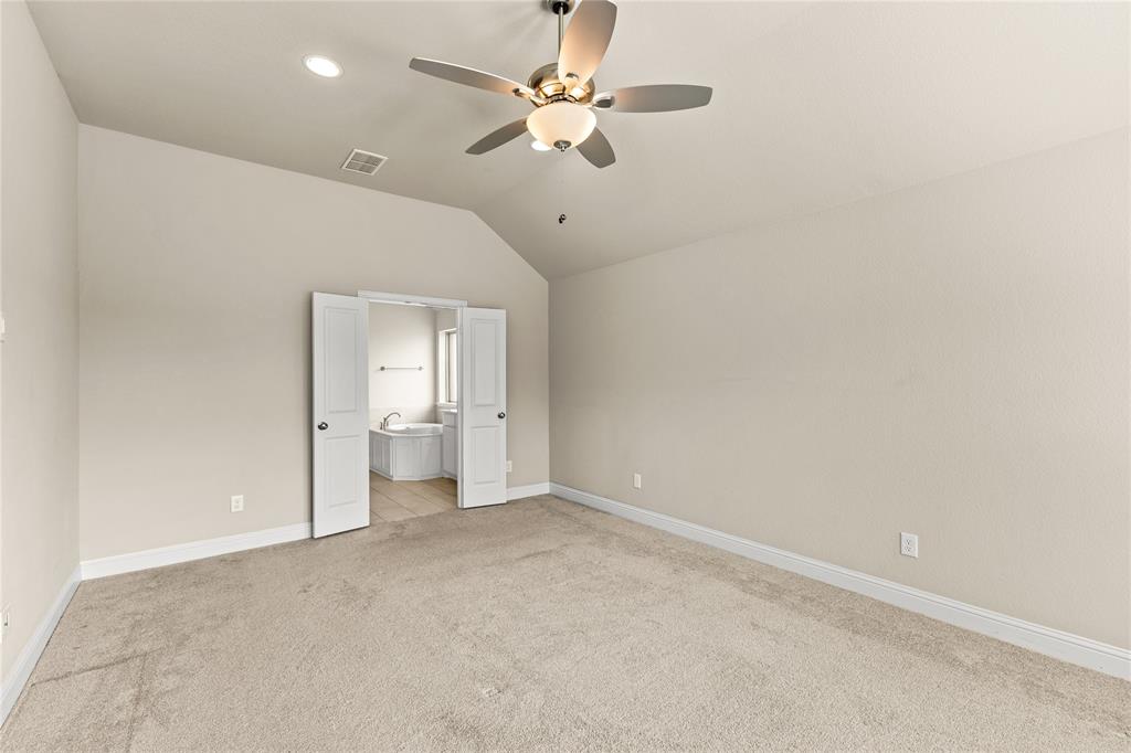 Vaulted ceiling featuring a central multi-blade ceiling fan with integrated light fixture, neutral wall finishes, and double doors opening to a space with tile flooring and a soaking tub