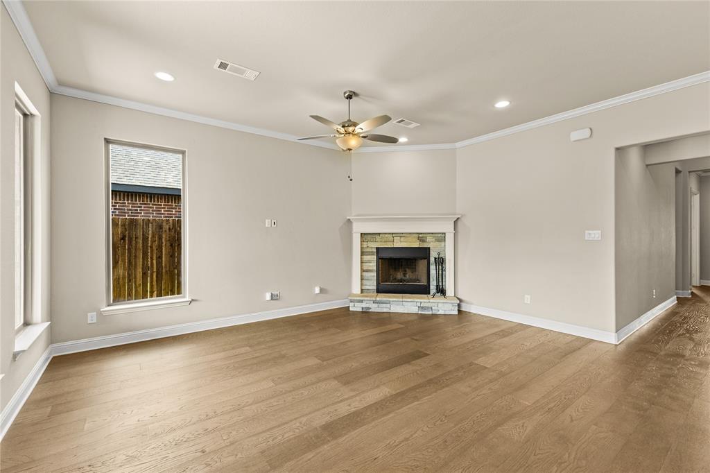Wood-finish flooring throughout with a corner stone-accented fireplace, wood-burning hearth, ceiling fan with integrated lighting, and recessed ceiling illumination
