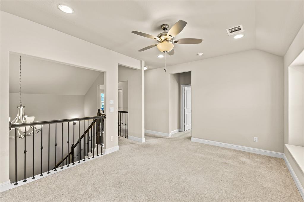 Vaulted ceiling, ceiling fan with light fixture, carpeted flooring, built-in window seat, and metal spindle railing