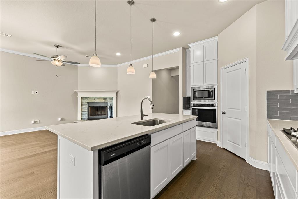 Kitchen featuring a central island with a quartz countertop, white cabinetry, integrated stainless steel appliances, and wood-finish flooring, complemented by a stone-faced fireplace