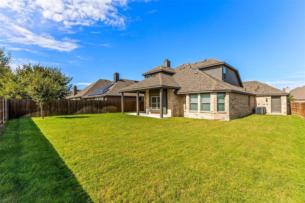 Brick and horizontal siding exterior featuring a covered patio, expansive lawn, and wood-panel perimeter fencing