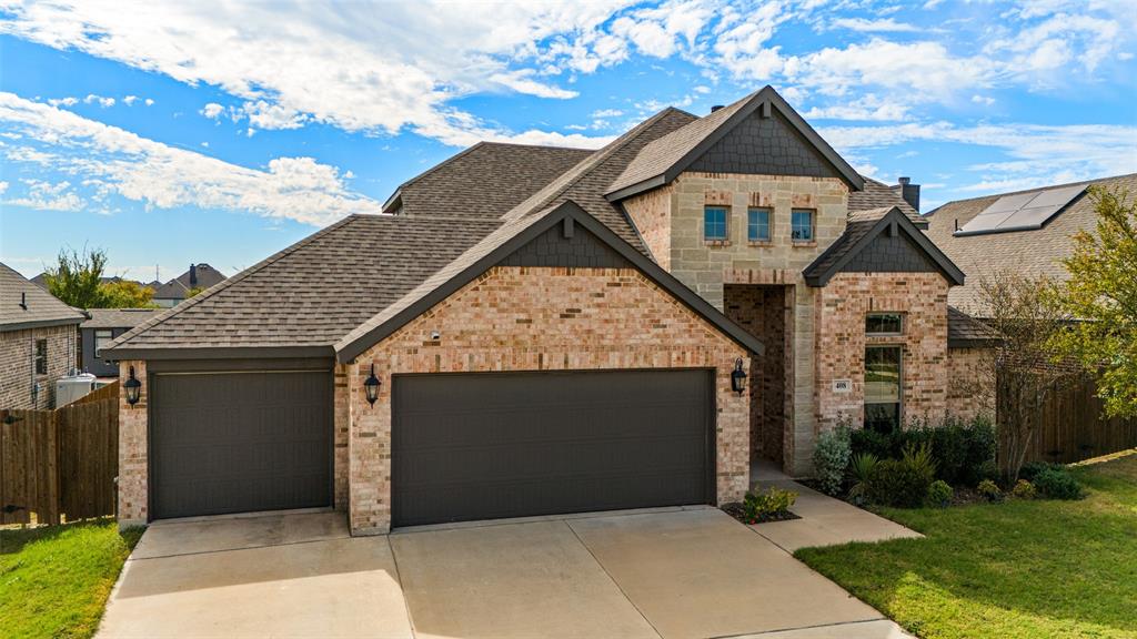 Multi-level exterior featuring a brick and stone facade, dual-bay garage, steep-pitched roofline with shingles, and decorative shingle siding accents