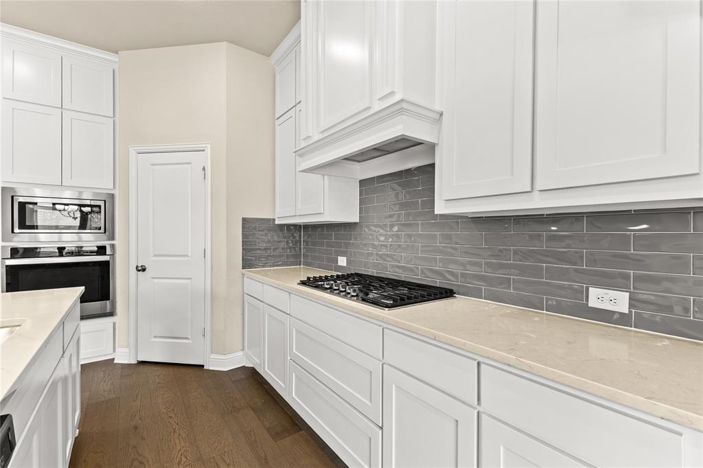 Kitchen featuring white shaker-style cabinetry, a gray subway tile backsplash, light-toned solid surface countertops, built-in stainless steel double wall ovens, and wood-finish flooring