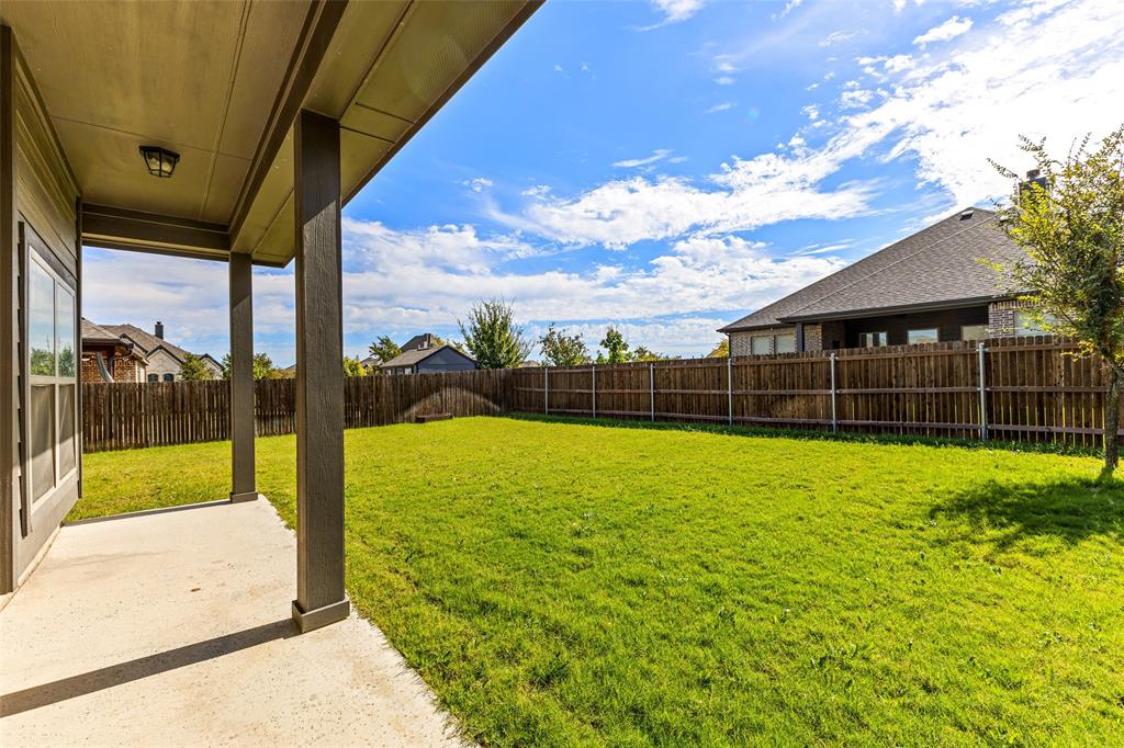Covered concrete patio with square support columns, fenced backyard, and established lawn